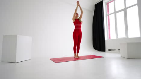 Beautiful-young-woman-wearing-red-sportswear-doing-yoga-or-pilates-exercise-pose-on-white-background.